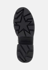 Suola di sneaker in gomma nera con motivo a stella, aree di presa testurizzate e logo "GUESS" in rilievo vicino al tallone.