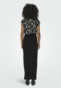 Jupe noire avec une taille ajustée et fente au dos, associée à un haut à manches courtes avec un motif ikat noir et blanc.