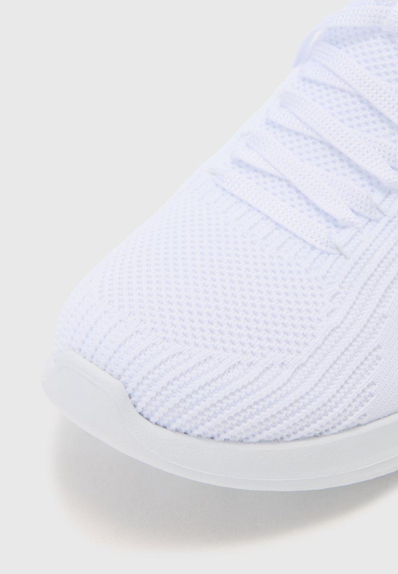 Scarpa atletica bianca con tomaia in rete traspirante e texture, con lacci e punta arrotondata. La suola è liscia e leggermente curva.