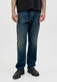 Blauwe denim jeans met een relaxte pasvorm, iets vervaagde voorkant en een klassiek vijf-pocket ontwerp; gecombineerd met zwarte schoenen.