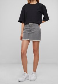 Černé zkrácené tričko, šedá džínová mini sukně s třepeným lemem a bílé tenisky. Jednoduchý, casual design s volným střihem.