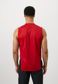 Piros ujjatlan sportpóló sima textúrával, ellentétes fehér részletekkel a vállakon, hátulról nézve.