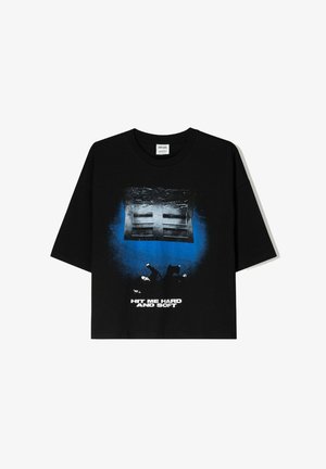 Fekete, oversize rövid ujjú póló, elöl kék és fehér grafikai nyomattal, amelyen az "ÜSD MEG ERŐSEN ÉS KELLEMESEN" felirat olvasható.