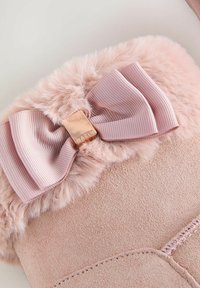 Stivale in suede rosa con un morbido risvolto in pelliccia, una texture trapuntata e un nastro di satin impreziosito da una chiusura metallica.