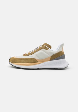 Lage sneaker met bovenwerk van witte mesh, beige suède overlays, beige accenten, witte veters en een dikke witte zool met een zwarte loopzool.