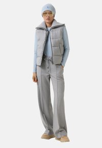 Gilet en duvet gris avec un col haut sur un haut à manches longues bleu clair, associé à un pantalon large gris et un bonnet en tricot bleu clair.