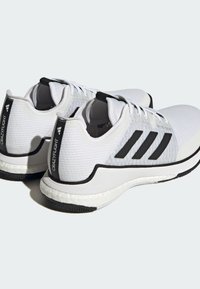Weiße Sportschuhe mit einer strukturierten Mesh-Oberfläche, schwarzen Streifenakzenten und einer gepolsterten Sohle. Sie sind mit einer markierten Fersenschlaufe und einer Schnürung ausgestattet.