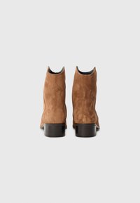 Botas de tobillo de ante marrón con una textura suave, punta redonda y tacones de goma negra. Presentan costuras decorativas en los laterales.