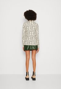 Top a maniche lunghe con un motivo composto da una base beige chiaro e forme geometriche nere, abbinato a una gonna in ecopelle verde scuro e stivaletti.