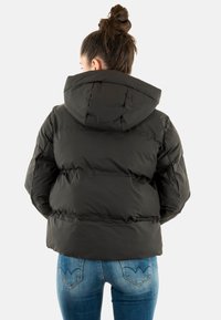 Sort dunjakke med hætte, quiltet tekstur og en firkantet pasform. Bær den over blå denimjeans med en synlig baglomme.