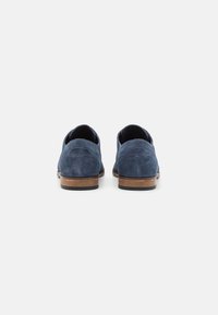 Zapatos de ante azul marino con una textura suave, tacón de madera y suela de goma negra contrastante; punta redondeada y diseño sin cordones.