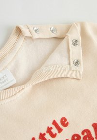 Beige Baby-Sweatshirt mit weicher Textur, rundem Halsausschnitt, Druckknöpfen am Kragen und rotem Schriftzug "little."