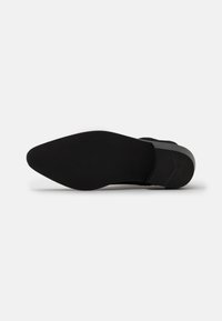 Suola nera di scarpa con design a punta. Materiale in gomma testurizzata, tacco leggermente rialzato e marchio sottile inciso sulla superficie.
