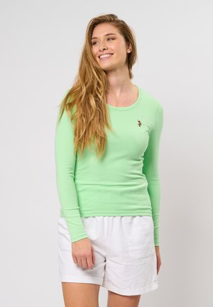 Lange mouw groene geribde top met een ronde hals, voorzien van een klein geborduurd ontwerp. Gecombineerd met witte shorts. Zachte textuur.