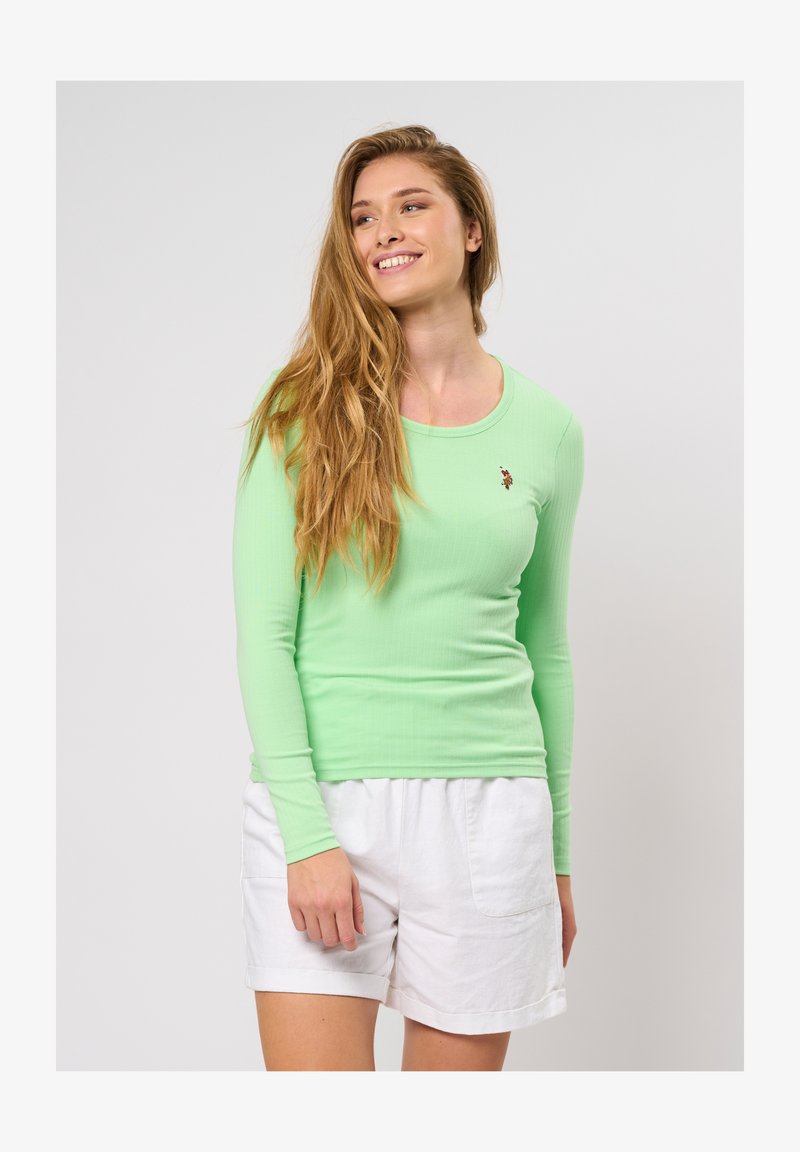 Garšas piedurkņu zaļa ribota blūze ar apaļu izgriezumu, kurai ir neliels izšuvums. Saskaņota ar baltām šortiem. Mīksta tekstūra.