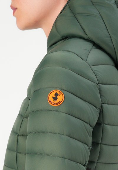 Personne portant une veste matelassée verte avec un patch circulaire orange représentant un canard et "SAVE THE DUCK" sur la manche supérieure gauche.