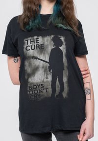 Black cotton t-shirt featuring a graphic design of a silhouetted figure holding a guitar, with "THE CURE" and "BOYS DON'T CRY" text.
