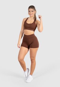 Bruine sportbeha en bijpassende high-waisted shorts van rekbare stof, met een gladde textuur en minimale branding op de borst.