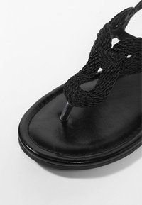 Sorte sandaler med en flad, glat lædersål, en flettet tekstilrem og en tæerem, designet til afslappet brug.