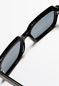 Czarne, oversize okulary przeciwsłoneczne z masywną plastikową oprawką, prostokątnym kształtem i ciemnymi przyciemnianymi soczewkami; z metalowymi akcentami przy zawiasach.