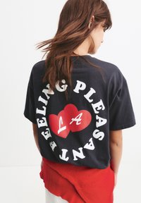Tricou din bumbac negru cu text alb și un grafic de inimă roșie cu "LA" în interior. Designul este centrat pe spate. Mâneci scurte, croială lejeră.
