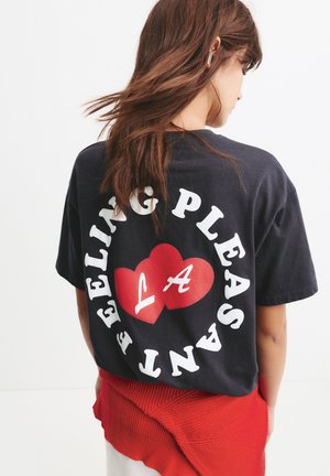 T-shirt in cotone nero con testo bianco e un grafiche cuore rosso con "LA" all'interno. Il design è centrato sul retro. Maniche corte, vestibilità comoda.