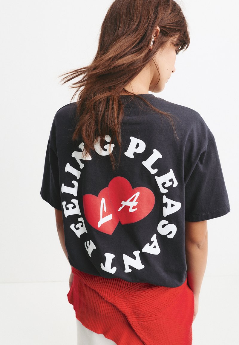 Tricou din bumbac negru cu text alb și un grafic de inimă roșie cu "LA" în interior. Designul este centrat pe spate. Mâneci scurte, croială lejeră.