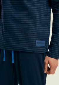 Granatowy, długi rękaw top z cienkimi niebieskimi paskami, z niebieską metką z napisem "HENDERSON" oraz dopasowanymi sznurkami u dołu.