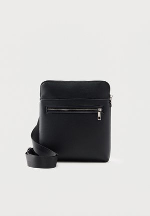 Sac bandoulière noir rectangulaire avec poche zippée à l'avant et sangle réglable sur fond blanc uni.