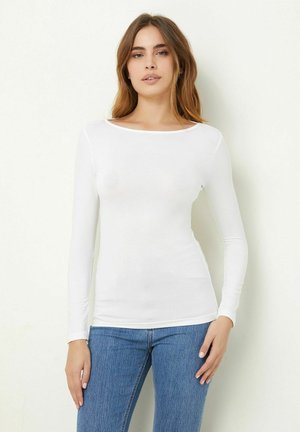 Hvid langærmet skjorte i en tætsiddende design, med rund halsudskæring og blød, strækbar tekstur, parret med blå denim jeans.