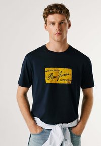 Marineblå bomuldst-shirt med en gul rektangulær grafik med teksten "DENIM BRAND" og "Pepe Jeans LONDON" i sort. Casual pasform.