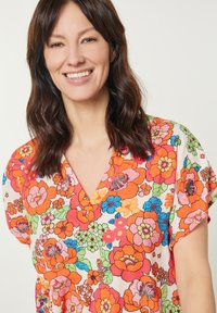 Blusa floreale con scollatura a V, maniche corte, in vivaci colori arancione, rosa e blu, realizzata in un tessuto testurizzato e decorato.