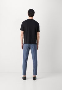 Zwarte korte mouwen shirt gecombineerd met lichtblauwe op maat gemaakte broeken. De outfit heeft een relaxte pasvorm en subtiele texturen, aangevuld met zwarte schoenen.