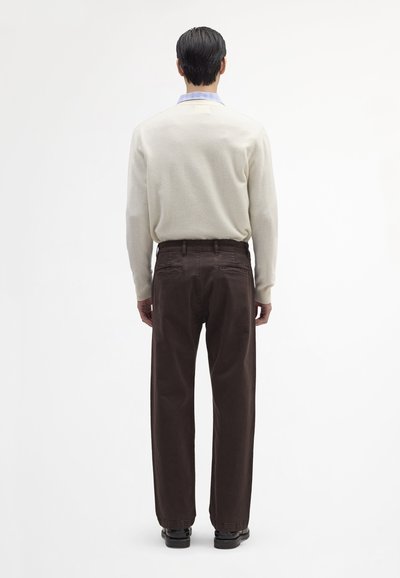 Pull gris clair à col rond, associé à un pantalon marron foncé. Le pantalon est doté de deux poches arrière et d'une coupe droite.