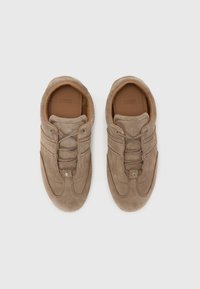 Chaussures en daim beige clair avec une texture lisse, dotées de lacets élastiques, d'un col rembourré et d'un logo en relief sur la semelle intérieure beige.
