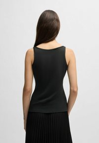 Top in cotone nero a coste, con un design aderente, spalline larghe e scollatura liscia, mostrato di retro su uno sfondo neutro.