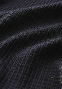 Tissu bleu marine avec un motif texturé et ondulé ; présente une surface douce et légèrement surélevée. Le matériau semble léger et lisse.