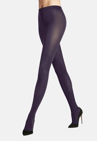 Modella che indossa collant trasparenti viola e tacchi alti neri, che assume una posa con una gamba in avanti, mettendo in mostra un outfit alla moda.