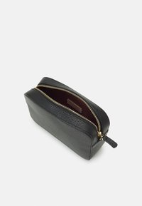 Borsa cosmetica in pelle nera con superficie texture. Presenta una chiusura con cerniera dorata e un rivestimento interno rosso scuro. Forma rettangolare.