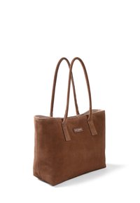 Sac fourre-tout en daim marron avec deux longues anses, forme rectangulaire, base plate et une plaque de logo en métal à l'avant. Texture lisse.