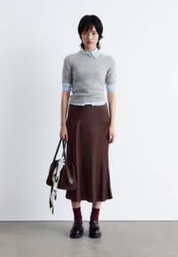 Grauer Kurzarmpullover über einem hellblauen Hemd mit Kragen, kombiniert mit einem braunen Satinrock. Braune Tasche mit einem schwarz-weißen Schal, schwarze Schuhe.