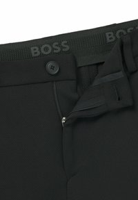 Pantaloni neri con tessuto testurizzato, chiusura con cerniera e bottone. La vita presenta il nome del marchio "BOSS" in lettere in rilievo.