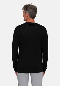 Zwarte longsleeve shirt gemaakt van lichtgewicht stof. Heeft een ronde halslijn en een wit logo op de achterkant, met aangesloten mouwen.
