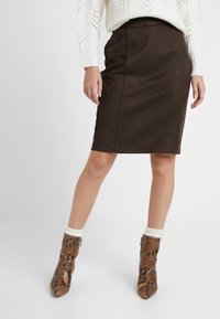 Hnědá semišová tužková sukni se slim fit střihem, která má čisté linie a hladkou texturu. Doplňena hnědými kotníkovými botami s hadím vzorem.