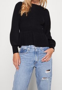 Haut en maille côtelée noire avec un ourlet évasé, un col rond et des manches longues. Associé à un jean taille haute bleu clair déchiré.