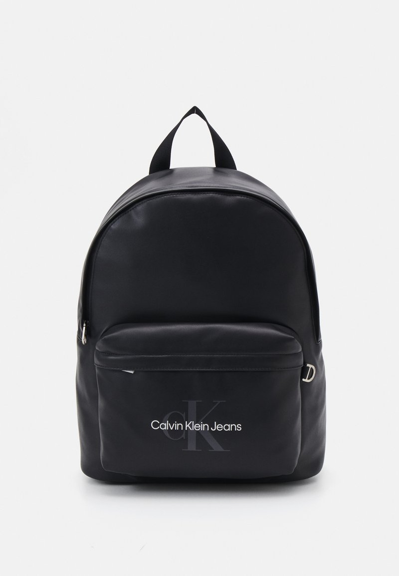 Zaino nero realizzato in materiale morbido, con una tasca anteriore con zip e un logo. Include spallacci in tessuto doppi e una parte superiore arrotondata.