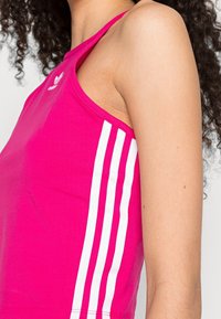 Rosa linne i bomull med vita tre-strimmor längs sidorna och en logotyp på bröstet. Ärmlös med rund halsringning.