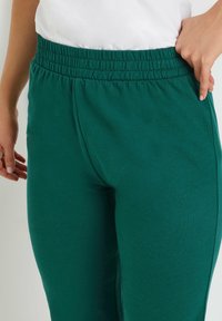 Groene katoenen joggers met een elastische tailleband. Ze hebben een zachte textuur en een aansluitende silhouette, met details aan de zijkant en tailleband.