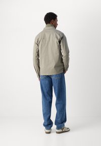 Jachetă gri deschis, din material de bumbac, guler cu nasturi, mâneci lungi, ușor ajustată cu linii pe spate. Purtați cu blugi largi din denim albastru și pantofi bej.