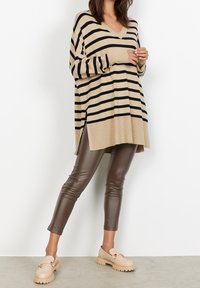 Beige en zwart gestreepte oversized trui met een V-hals, gecombineerd met strakke bruine neplederen broeken en beige robuuste loafers.
